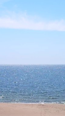 Sea, white sun reflections, yellow sandy beach and blue sky on hot sunny summer day. Sun shines on sea water on coast. Beautiful natural background. Seamless Looping Vertical video