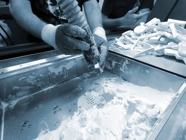 A man working with a working vacuum cleaner to clean the white powder of polyamide from a model printed on a 3D printer inside a 3D printer. Cleaning objects printed on an industrial powder 3D printer