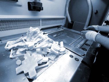 Adam, endüstriyel 3D yazıcıda beyaz plastik tozdan basılmış detayları temizliyor. Otomatik katkı teknolojileri. Kişi, 3 boyutlu yazıcıda basılan modellerden elektrikli süpürge tozunu temizliyor.