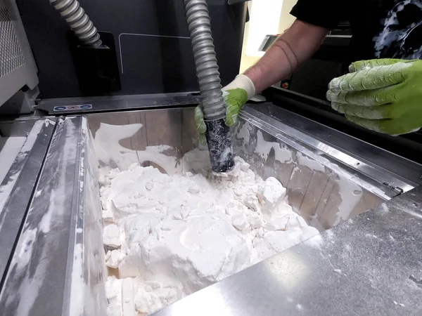 A man working with a working vacuum cleaner to clean the white powder of polyamide from a model printed on a 3D printer inside a 3D printer. Cleaning objects printed on an industrial powder 3D printer