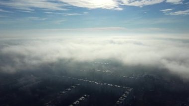 Aerial drone view flight over clouds fog mist, buildings roof in city and under white clouds in blue sky on sunny day. Abstract natural urban background. Atmosphere. Top view fog cloudy and rooftops