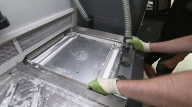 Bir erkek işçi, elektrikli süpürgeyle endüstriyel 3D yazıcının yüzeyini beyaz tozdan temizliyor. Çoklu Jet Füzyon MJF 3D baskı. Çalışma süreci