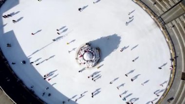 Birçok insan güneşli bir kış gününde beyaz bir açık hava buz pateni pistinde kayıyor. Beyaz bir buz pateni pistinin yüzeyinde kayan insanların gölgeleri. Hava aracı görüntüsü. Üst Manzara. Yaşam tarzı, spor, dinlenme