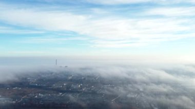 Aerial drone view flight over clouds fog mist, buildings, industrial area in city and under white clouds in blue sky day. Abstract natural urban background. Atmosphere. Top view fog cloudy and town