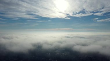 Aerial drone view flight over clouds fog mist, buildings roof in city and under white clouds in blue sky on sunny day. Abstract natural urban background. Atmosphere. Top view fog cloudy and rooftops