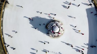 Birçok insan güneşli bir kış gününde beyaz bir açık hava buz pateni pistinde kayıyor. Beyaz bir buz pateni pistinin yüzeyinde kayan insanların gölgeleri. Hava aracı görüntüsü. Üst Manzara. Yaşam tarzı, spor, dinlenme