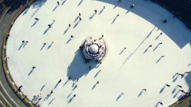 Birçok insan güneşli bir kış gününde beyaz bir açık hava buz pateni pistinde kayıyor. Beyaz bir buz pateni pistinin yüzeyinde kayan insanların gölgeleri. Hava aracı görüntüsü. Üst Manzara. Yaşam tarzı, spor, dinlenme