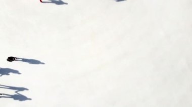 Birçok insan güneşli bir kış gününde beyaz bir açık hava buz pateni pistinde kayıyor. Beyaz bir buz pateni pistinin yüzeyinde kayan insanların gölgeleri. Hava aracı görüntüsü. Üst Manzara. Yaşam tarzı, spor, dinlenme