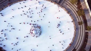 Many people are skating on a white outdoor ice rink in the city on winter day. People skating on the surface of a white ice rink. Aerial drone view. Top view. Lifestyle, sport, rest