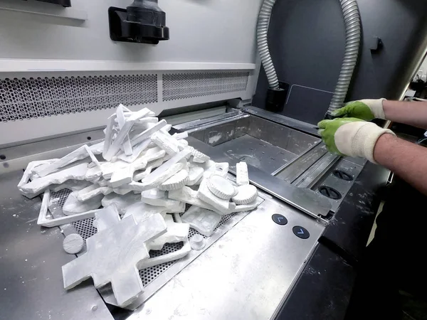 Man cleans details printed on industrial 3D printer from white plastic powder. Automated additive technologies. Person cleans vacuum cleaner plastic powder from models printed on 3D printer. Top view