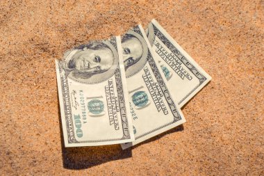 Kumsalda kumla kaplanmış paranın yarısı yakın planda duruyor. Dolar banknotları kısmen kuma gömülmüş. Okyanus sahilinde kumlara gömülü 300 dolar. Finans parası hariç. Tatilde rahatla.