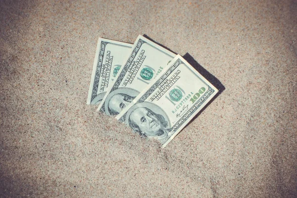 Money dolars half covered with sand lie on beach close-up. Three hundred dollars buried in sand on sea or ocean beach Concept finance money holiday relax vacation. Sunny summer warm wind day.