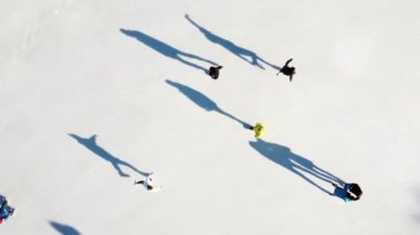 Birçok insan güneşli bir kış gününde beyaz bir açık hava buz pateni pistinde kayıyor. Beyaz bir buz pateni pistinin yüzeyinde kayan insanların gölgeleri. Hava aracı görüntüsü. Üst Manzara. Yaşam tarzı, spor, dinlenme