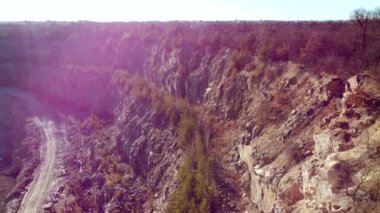 Rocks wall of granite stone quarry top view. Aerial drone view over sheer granite wall cliff overgrown with trees in grant quarry. Industrial quarry for extraction of granite. Landscape. Red sun glare