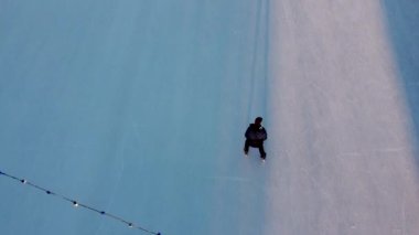 Man skating on an open-air ice skating rink in the city in the evening during sunset in winter. Top view. People skating on ice rink. Long shadows of people on surface of ice. View from above