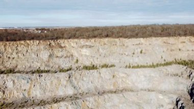 Granite rocky stone wall and many trees growing on it of granite quarry on sunny day. Aerial drone view. Flying over a rocky huge cliff wall created in a granite quarry. Heavy mining industry