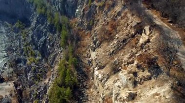 Rocks wall of granite stone quarry top view. Aerial drone view over sheer granite wall cliff overgrown with trees in grant quarry. Industrial quarry for extraction of granite. Landscape on sunny day