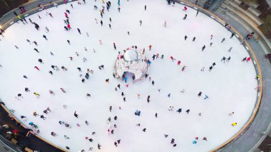 Many people are skating on a white outdoor ice rink in the city on winter day. People skating on the surface of a white ice rink. Aerial drone view. Top view. Lifestyle, sport, rest
