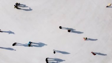 Birçok insan güneşli bir kış gününde beyaz bir açık hava buz pateni pistinde kayıyor. Beyaz bir buz pateni pistinin yüzeyinde kayan insanların gölgeleri. Hava aracı görüntüsü. Üst Manzara. Yaşam tarzı, spor, dinlenme