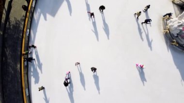 Birçok insan güneşli bir kış gününde beyaz bir açık hava buz pateni pistinde kayıyor. Beyaz bir buz pateni pistinin yüzeyinde kayan insanların gölgeleri. Hava aracı görüntüsü. Üst Manzara. Yaşam tarzı, spor, dinlenme