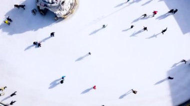 Birçok insan güneşli bir kış gününde beyaz bir açık hava buz pateni pistinde kayıyor. Beyaz bir buz pateni pistinin yüzeyinde kayan insanların gölgeleri. Hava aracı görüntüsü. Üst Manzara. Yaşam tarzı, spor, dinlenme