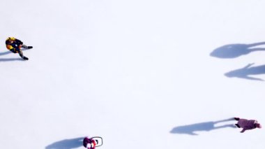 Birçok insan güneşli bir kış gününde beyaz bir açık hava buz pateni pistinde kayıyor. Beyaz bir buz pateni pistinin yüzeyinde kayan insanların gölgeleri. Hava aracı görüntüsü. Üst Manzara. Yaşam tarzı, spor, dinlenme