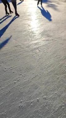 People skating on public open-air ice skating rink in city on sunny winter day. People skating on ice rink. Legs, back, shadows, sunlight ice rink. Winter holidays activities rest. Vertical video
