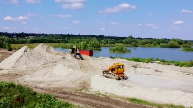 Chepelievka, Ukraine, August 25, 2021:-Aerial drone view flight over sand mining. Sand quarry. Sand pit and lake with blue water. Excavator scoops up sand. Bulldozer machine moving ground.