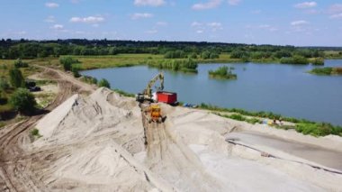 Chepelievka, Ukraine, August 25, 2021:-Aerial drone view flight over sand mining. Sand quarry. Top view. Lake with blue water near sand pit. Bulldozer machine moving sand in quarry. Mining industry.