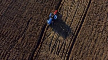 A man on tractor digging the ground. Tractor driver plowing the field. A worker on blue tractor digs up the brown earth. Aerial drone view. Top view. Farming countryside rural. Agrarian. Agricultural