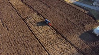 A man on tractor digging the ground. Tractor driver plowing the field. A worker on blue tractor digs up the brown earth. Aerial drone view. Top view. Farming countryside rural. Agrarian. Agricultural