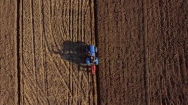 A man on tractor digging the ground. Tractor driver plowing the field. A worker on blue tractor digs up the brown earth. Aerial drone view. Top view. Farming countryside rural. Agrarian. Agricultural