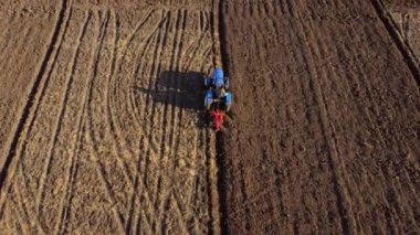 A man on tractor digging the ground. Tractor driver plowing the field. A worker on blue tractor digs up the brown earth. Aerial drone view. Top view. Farming countryside rural. Agrarian. Agricultural