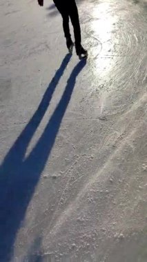 People skating on public open-air ice skating rink in city on sunny winter day. People skating on ice rink. Legs, back, shadows, sunlight ice rink. Winter holidays activities rest. Vertical video