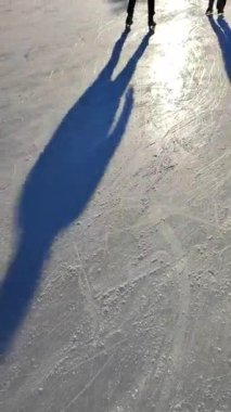People skating on public open-air ice skating rink in city on sunny winter day. People skating on ice rink. Legs, back, shadows, sunlight ice rink. Winter holidays activities rest. Vertical video