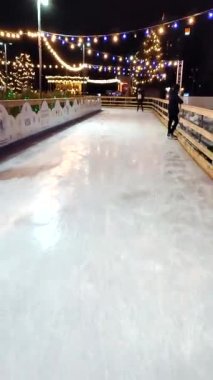 Kyiv, Ukraine, January 3, 2022: People skating on public open-air ice skating rink in city on winter night. New Year Christmas holidays, decorations illumination garlands flashlights. Vertical video