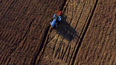 A man on tractor digging the ground. Tractor driver plowing the field. A worker on blue tractor digs up the brown earth. Aerial drone view. Top view. Farming countryside rural. Agrarian. Agricultural