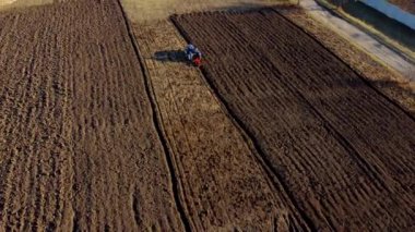 A man on tractor digging the ground. Tractor driver plowing the field. A worker on blue tractor digs up the brown earth. Aerial drone view. Top view. Farming countryside rural. Agrarian. Agricultural