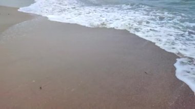 Deniz kıyısının kumlu sahilinde beyaz köpüklü dalgalar yuvarlanıyor. Kum, tropikal ve egzotik sahil şeridi. Deniz dalgaları yakın çekim. Deniz kıyısında. Doğal arka plan. Yaz doğa arka planı.