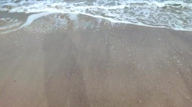Deniz kıyısının kumlu sahilinde beyaz köpüklü dalgalar yuvarlanıyor. Kum, tropikal ve egzotik sahil şeridi. Deniz dalgaları yakın çekim. Deniz kıyısında. Doğal arka plan. Yaz doğa arka planı.