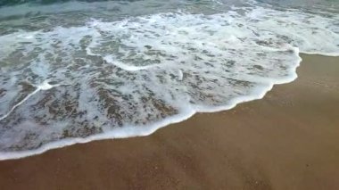 Deniz kıyısının kumlu sahilinde beyaz köpüklü dalgalar yuvarlanıyor. Kum, tropikal ve egzotik sahil şeridi. Deniz dalgaları yakın çekim. Deniz kıyısında. Doğal arka plan. Yaz doğa arka planı.