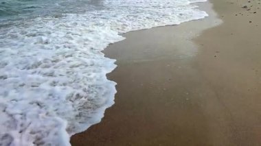 Deniz kıyısının kumlu sahilinde beyaz köpüklü dalgalar yuvarlanıyor. Kum, tropikal ve egzotik sahil şeridi. Deniz dalgaları yakın çekim. Deniz kıyısında. Doğal arka plan. Yaz doğa arka planı.