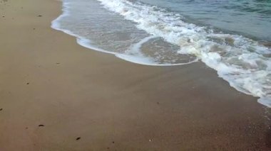 Deniz kıyısının kumlu sahilinde beyaz köpüklü dalgalar yuvarlanıyor. Kum, tropikal ve egzotik sahil şeridi. Deniz dalgaları yakın çekim. Deniz kıyısında. Doğal arka plan. Yaz doğa arka planı.