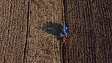 A man on tractor digging the ground. Tractor driver plowing the field. A worker on blue tractor digs up the brown earth. Aerial drone view. Top view. Farming countryside rural. Agrarian. Agricultural