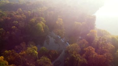 Güneşli bir sonbahar sabahında, göl üzerinde kuğular, mimari sütunlar ve sarı-yeşil yapraklı ağaçlarla hava aracı görüntüsü. Güneş ışınları, kırmızı güneş ışığı, güneşe aşırı maruz kalma. Doğal arkaplan
