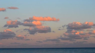 Zaman ayarlı. Günbatımında hareket eden kırmızı-turuncu bulutlar denizin üzerinde şafak vakti gökyüzünde. Deniz seviyesinin üzerinde gün batımının kırmızı turuncu ışığıyla aydınlanan bulutlar. Güzel doğal arkaplan