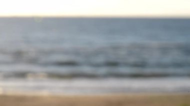 Arka plan bulanık. Yaz güneşli sabahında kumlu sahilde beyaz köpüklü deniz dalgası. Doğal bulanık bokeh dokusu arkaplanı. Güzel doğal arka plan. Çevre, küresel ısınma, iklim değişikliği