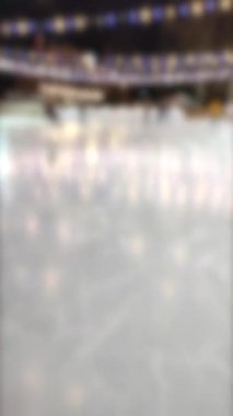 Blurred background. People skating on public open-air ice skating rink in city on winter night. Winter New Year Christmas holidays, decorations illumination garlands flashlights. Vertical video