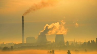 Gün batımında şehir manzarası silueti duman fabrikası. Endüstri kirliliği. Büyük yuvarlak baca, beyaz sigara ve elektrik direği çıkıyor.