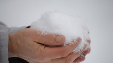 Yaşlı bir adam ellerini karda yakın planda tutuyor.